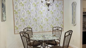 A dining area with a round table, six chairs, a chandelier, floral wallpaper, and a mirror. - Modern 2BR | Near Victoria Hospital (London)