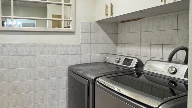 A laundry area with two front-loading washers, a window, and a tiled backsplash. - Modern 2BR | Near Victoria Hospital (London)