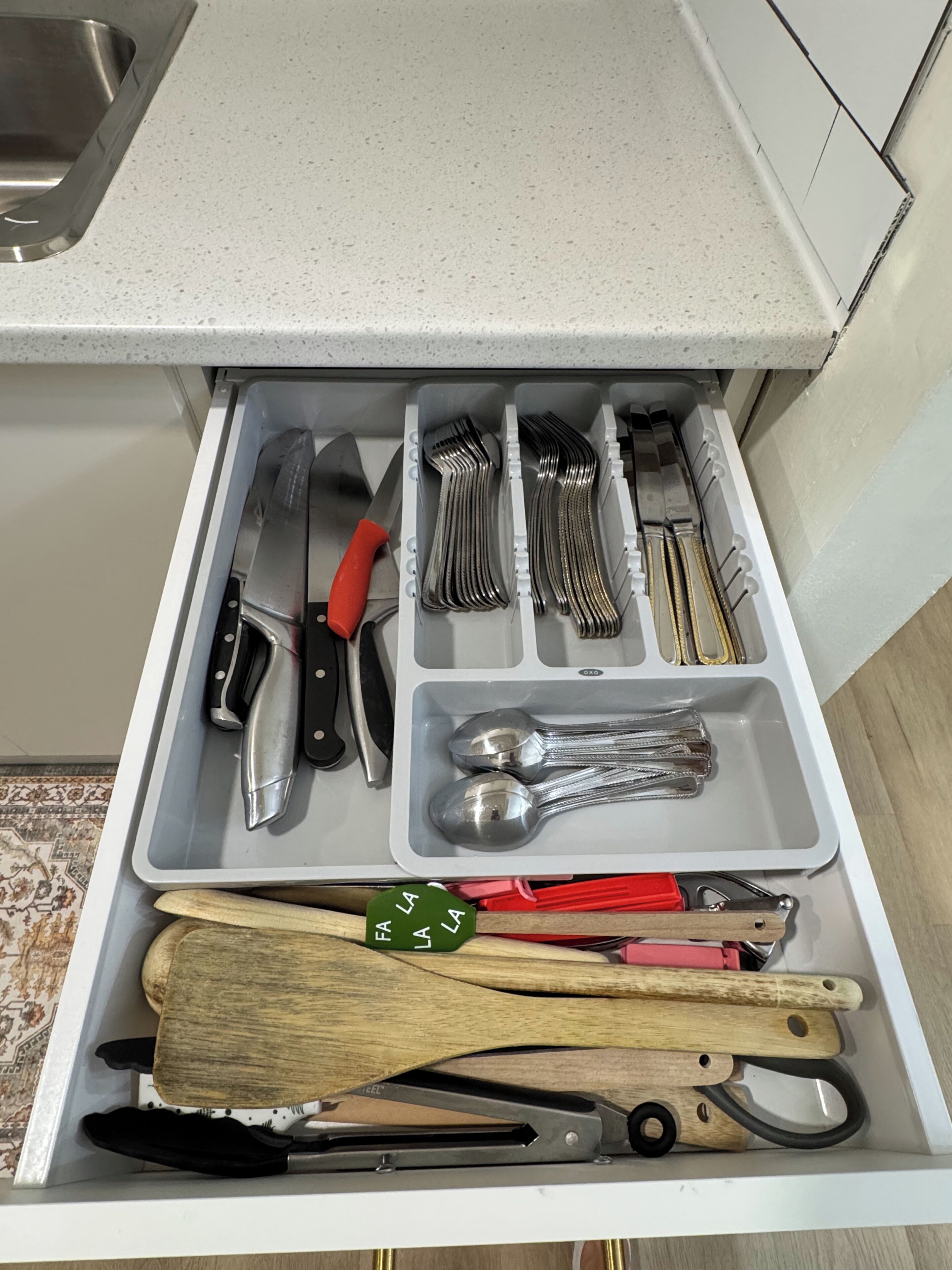 A kitchen drawer with utensils, including knives, forks, and spoons, organized in compartments.