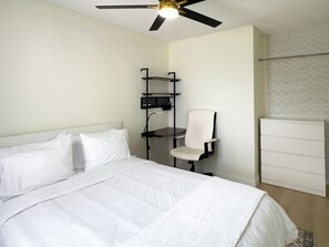 A hotel room with a bed, a desk, a chair, a wardrobe, and a ceiling fan. - Modern 2BR | Near Victoria Hospital (London)