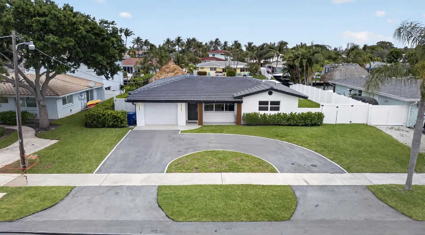 A residential house with a driveway, a lawn, and a white fence.