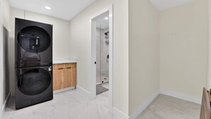 A modern laundry room with a washer and dryer, a wooden cabinet, and a glass shower door. - Cabana Retreat Private Dock (Pompano Beach)