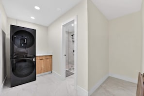 A modern laundry room with a washer and dryer, a wooden cabinet, and a glass shower door. - Cabana Retreat Private Dock (Pompano Beach)