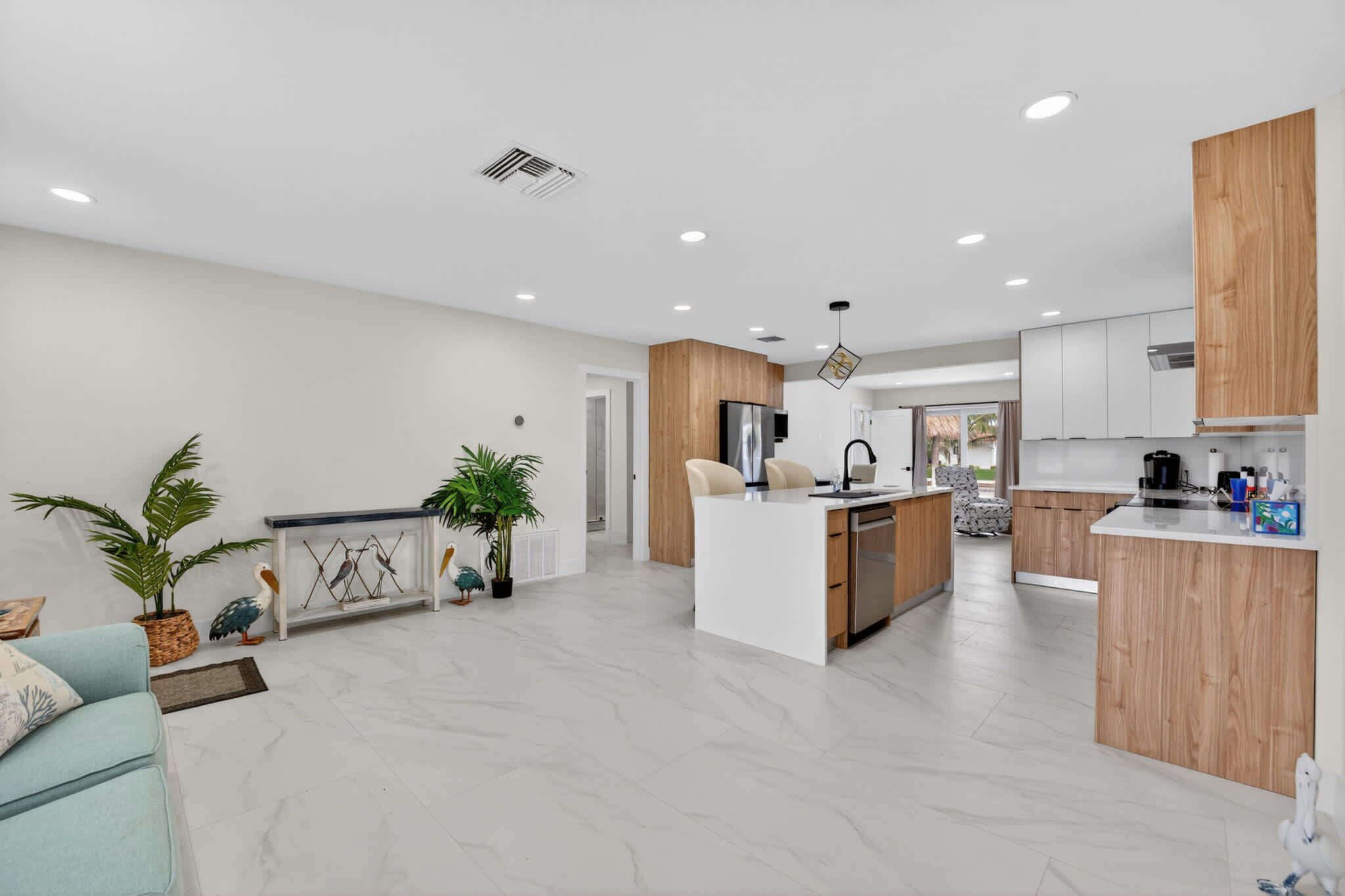 A modern kitchen with a central island, wooden cabinets, and a dining area with a light blue sofa.