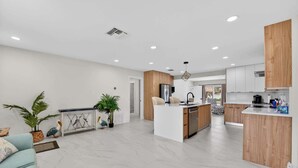 A modern kitchen with a central island, wooden cabinets, and a dining area with a light blue sofa. - Cabana Retreat Private Dock (Pompano Beach)