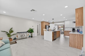 A modern kitchen with a central island, wooden cabinets, and a dining area with a light blue sofa. - Cabana Retreat Private Dock (Pompano Beach)