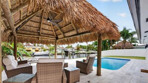 A covered outdoor seating area with wicker furniture, a pool, and a view of a marina. - Cabana Retreat Private Dock (Pompano Beach)