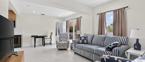 A modern living room with a sofa, armchair, and TV, a wooden table, and a small side table with a lamp.