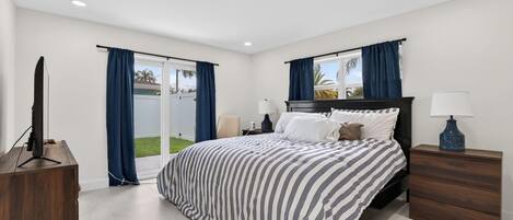 Un dormitorio con cama, mesita de noche, mueble para televisión y ventana con cortinas.
