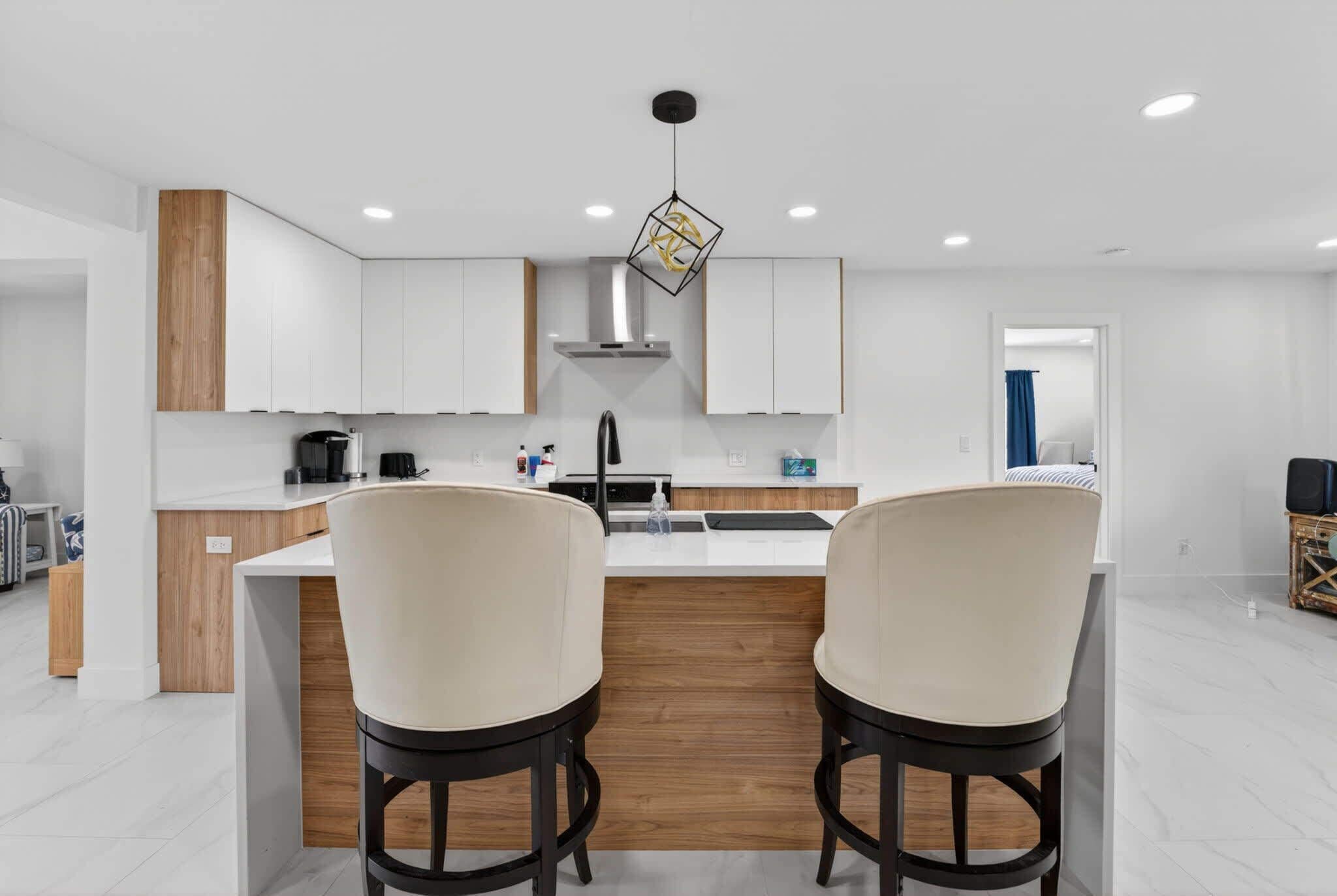 A modern kitchen with white cabinets, a wooden accent wall, a central island with two bar stools, and a pendant light.