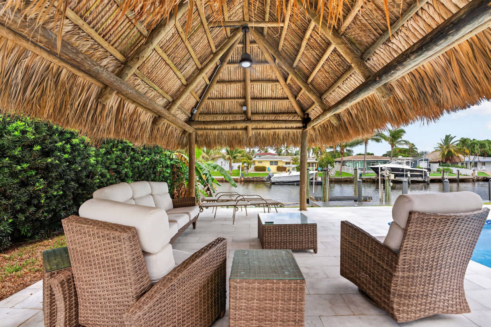 A covered outdoor seating area with wicker furniture, a thatched roof, and a view of a marina.