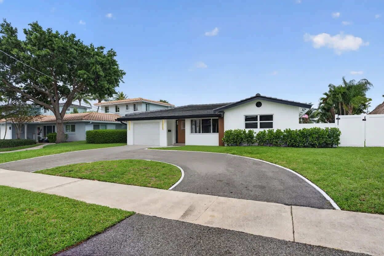 A residential house with a curved driveway, a front lawn, and a tree.