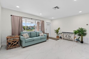A spacious living room with a light blue sofa, a wooden side table, a console table with decorative items, and potted plants. - Cabana Retreat Private Dock (Pompano Beach)