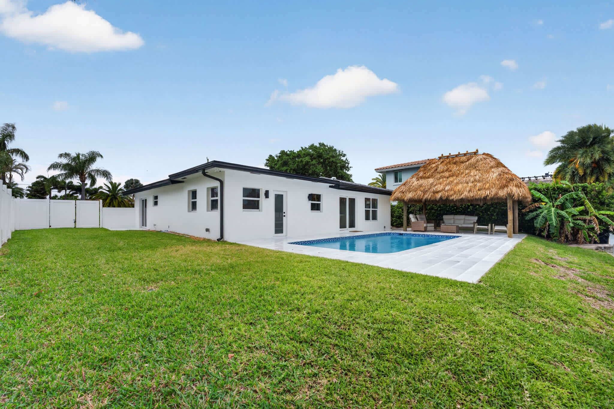 A house with a swimming pool, a thatched-roof structure, and a well-maintained lawn.