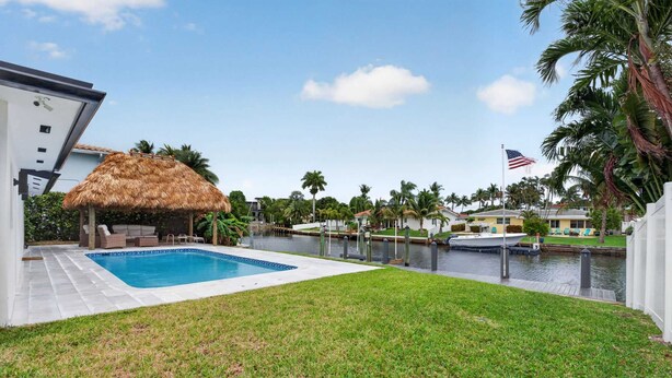A swimming pool, a thatched-roof structure, and a waterfront view with a flag. - Cabana Retreat Private Dock (Pompano Beach)