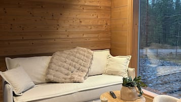 Une pièce chaleureuse avec un plafond en bois, un canapé agrémenté de coussins, une petite table ronde avec une télécommande, une bougie et une plante en pot.