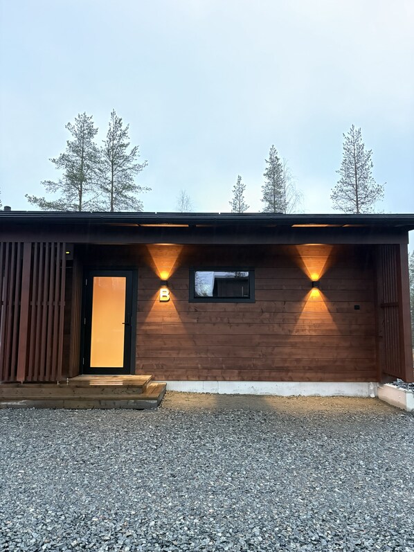 A wooden building with a black door and two illuminated wall sconces.