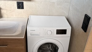 Une petite buanderie moderne, dotée d’un lave-linge encastré, d’un évier et de meubles de rangement en bois.