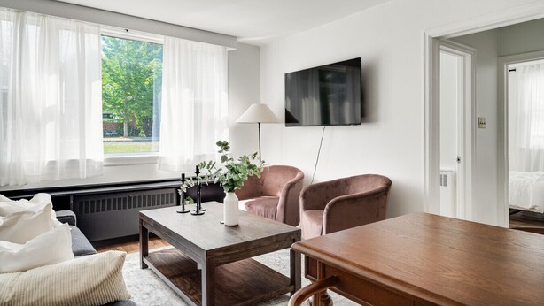 Habitación moderna con un ventanal grande, un televisor de pantalla plana, una mesa de madera, dos sillas y un radiador.