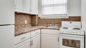 Una cocina con gabinetes blancos, salpicadero de ladrillo, pileta de acero inoxidable y estufa blanca.