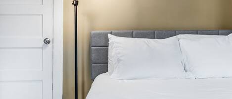 A hotel room with a bed, a nightstand, a lamp, and a door.