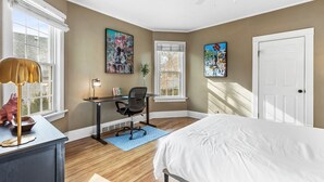 Une chambre à coucher avec un lit, un bureau, une chaise et des œuvres d’art accrochées aux murs.