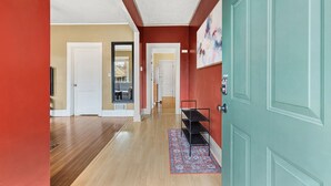 Un couloir avec un plancher en bois, un mur rouge et une porte turquoise. On y trouve une étagère noire et un tapis sur le sol.