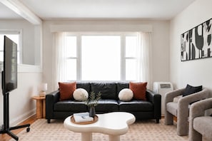 A living room with a black leather sofa, a white coffee table, and a grey armchair. - Cozy 2BR – Walk to Downtown & University! (Kingston)