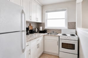 A kitchen with white cabinets, a stainless steel sink, a stove, and a window above the sink. - Cozy 2BR – Walk to Downtown & University! (Kingston)