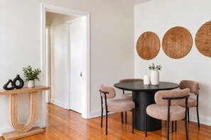 Un comedor con una mesa redonda, cuatro sillas, una consola con jarrones y tres adornos colgantes.