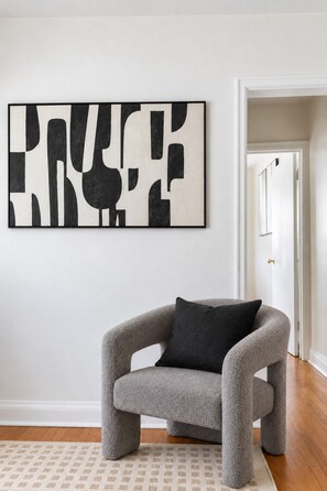 A room with a grey armchair, a patterned rug, and a large abstract artwork on the wall.