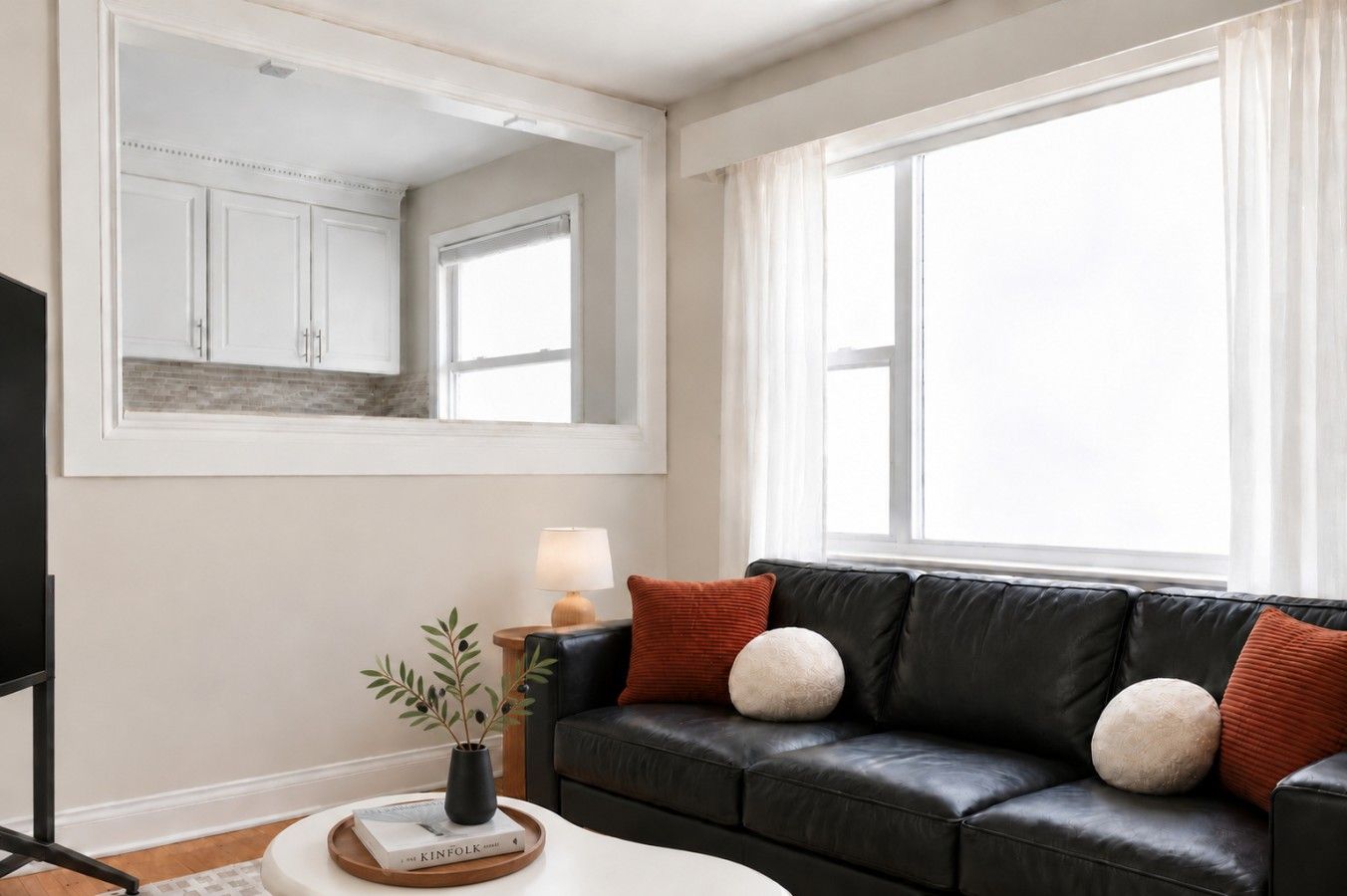 A living room with a black leather sofa, a side table with a lamp, a framed picture, and a potted plant.