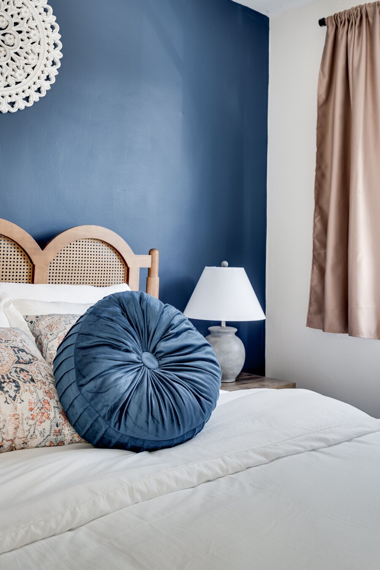 A bedroom with a bed, pillows, a headboard, a lamp, and a curtain.