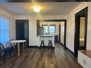 A compact room with a dining table, two stools, a kitchenette, and a bed in the adjacent room. - Peaceful Craftsman Home Near LBCC • Yard & Parking (Long Beach)