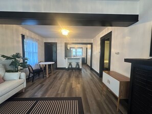 A modern living room with a sofa, a dining table, and a kitchen area with a counter and stools. - Peaceful Craftsman Home Near LBCC • Yard & Parking (Long Beach)