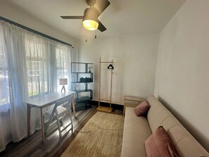 A modern living room with a sofa, a dining table with chairs, a standing lamp, and a ceiling fan. - Peaceful Craftsman Home Near LBCC • Yard & Parking (Long Beach)