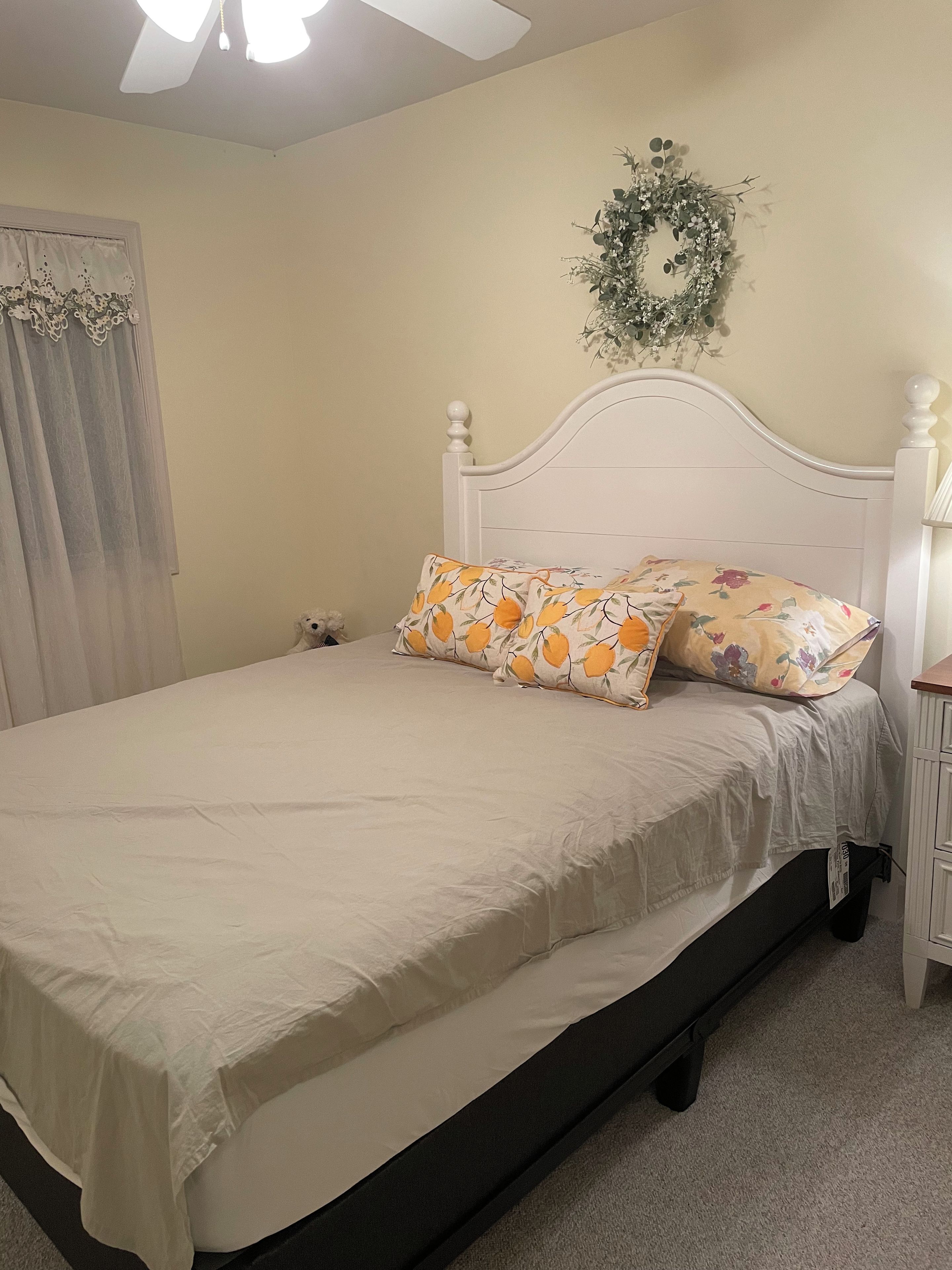 Quarto com cama, mesa de cabeceira, luminária na parede, ventilador de teto e uma guirlanda decorativa.