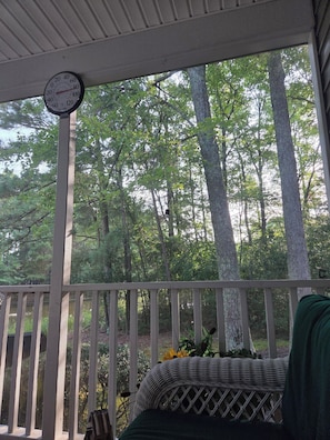 A covered porch with a clock, a wicker chair, and a view of a forest. - Homey 3-bedroom condo in cul-de-sac in Bethany Beach golf community (Bethany Beach)