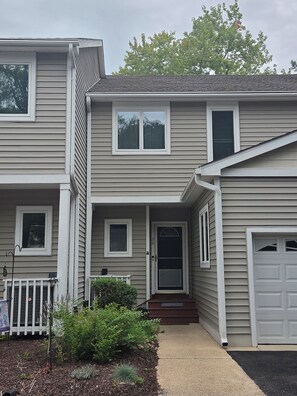 A two-story residential house with a front porch, a garage, and a small front yard with landscaping. - Homey 3-bedroom condo in cul-de-sac in Bethany Beach golf community (Bethany Beach)