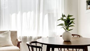 Ein Essbereich mit einem runden Tisch, Holzstühlen, einem weißen Sofa und durchscheinenden Vorhängen.