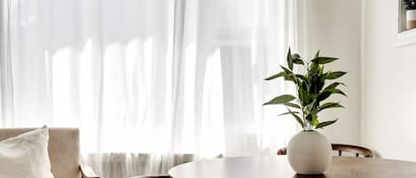 Un comedor con una mesa redonda, sillas de madera, un sofá blanco y cortinas translúcidas.