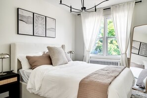 Un dormitorio con cama, mesitas de noche, una ventana con cortinas y decoración en la pared.