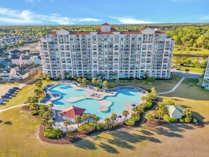 A large hotel with multiple balconies, a central swimming pool, and surrounding greenery. - Coastal Comfort Pet Friendly Barefoot Resort Villa (North Myrtle Beach)