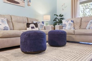 A living room with two beige sofas, a coffee table, and two blue ottomans. - Coastal Comfort Pet Friendly Barefoot Resort Villa (North Myrtle Beach)