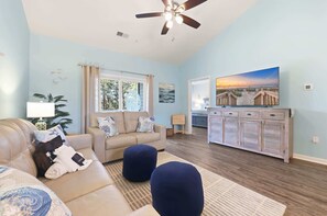 A living room with a beige sofa, blue ottomans, a ceiling fan, and a painting of a beach scene. - Coastal Comfort Pet Friendly Barefoot Resort Villa (North Myrtle Beach)