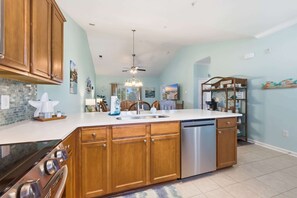 Une cuisine avec des meubles de rangement en bois, un lave-vaisselle, une cuisinière et un ventilateur de plafond.