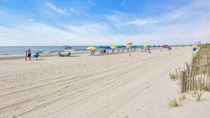 A beach with rows of umbrellas and chairs, a sandy shore, and the ocean in the background. - Coastal Comfort Pet Friendly Barefoot Resort Villa (North Myrtle Beach)