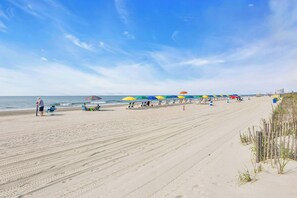 A beach with rows of umbrellas and chairs, a sandy shore, and the ocean in the background. - Coastal Comfort Pet Friendly Barefoot Resort Villa (North Myrtle Beach)