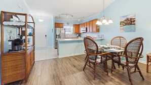 A kitchen with wooden cabinets, a dining table with wicker chairs, and a hanging light fixture. - Coastal Comfort Pet Friendly Barefoot Resort Villa (North Myrtle Beach)