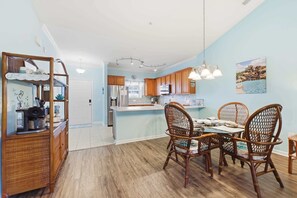 A kitchen with wooden cabinets, a dining table with wicker chairs, and a hanging light fixture. - Coastal Comfort Pet Friendly Barefoot Resort Villa (North Myrtle Beach)